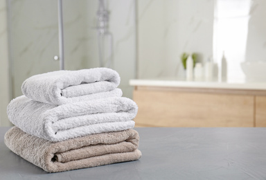 Stack of clean towels on grey stone table in bathroom. Space for text