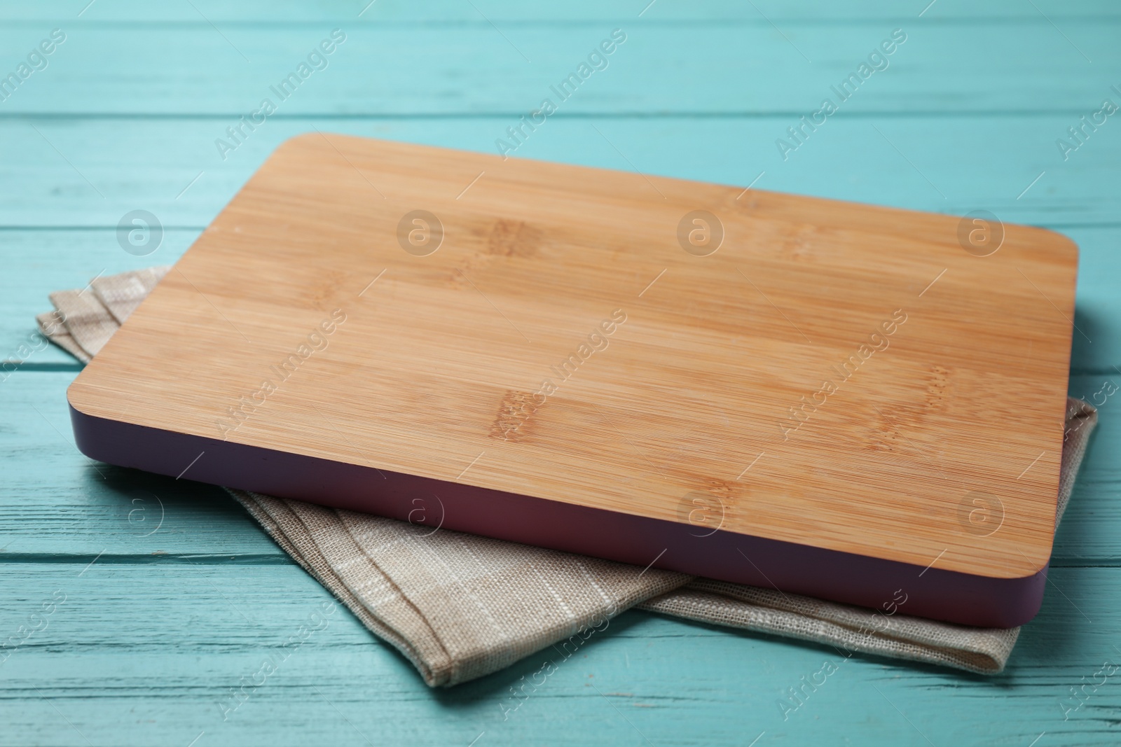 Photo of Wooden board and beige kitchen towel on blue table