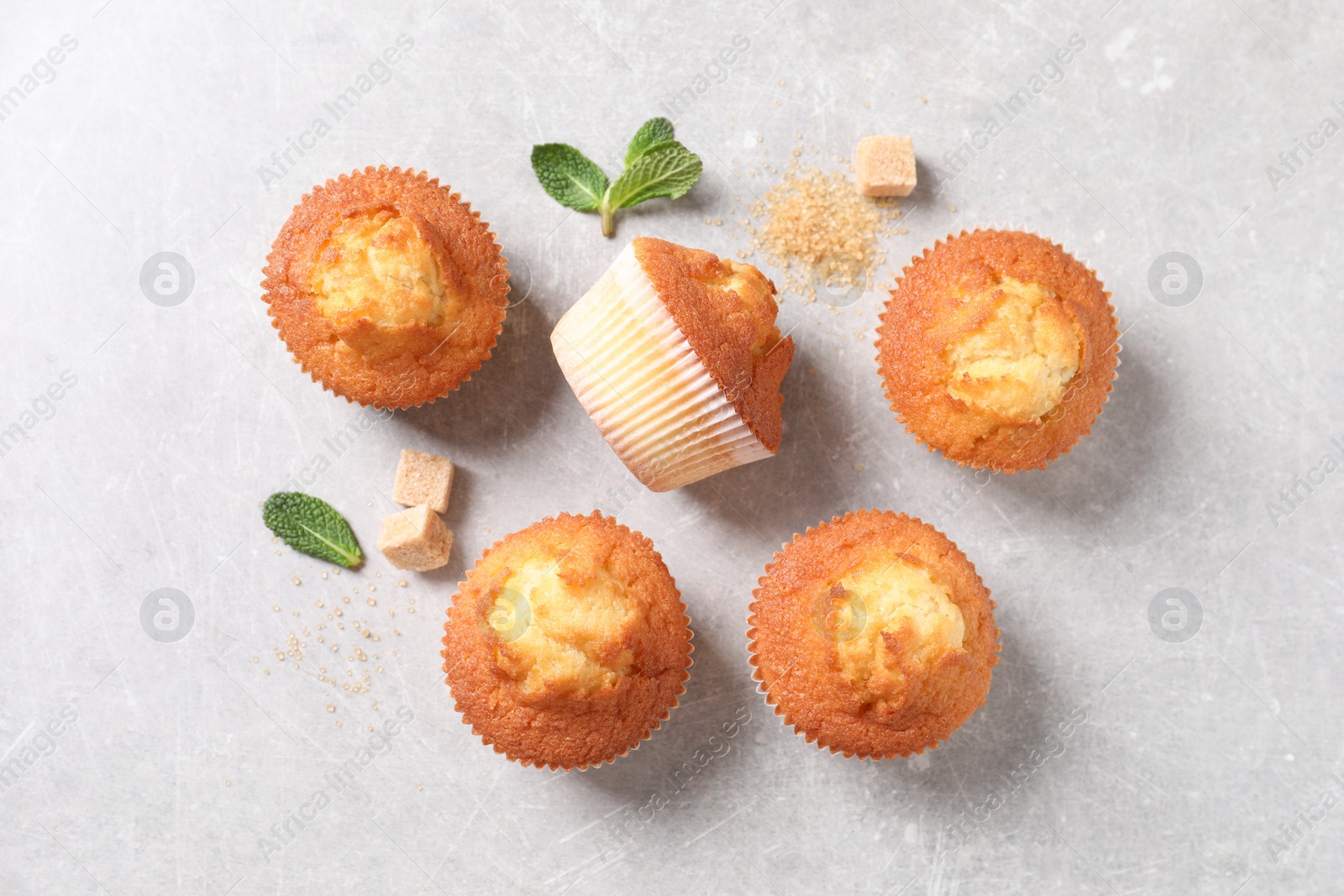 Photo of Delicious sweet muffins and brown sugar on light grey textured table, flat lay