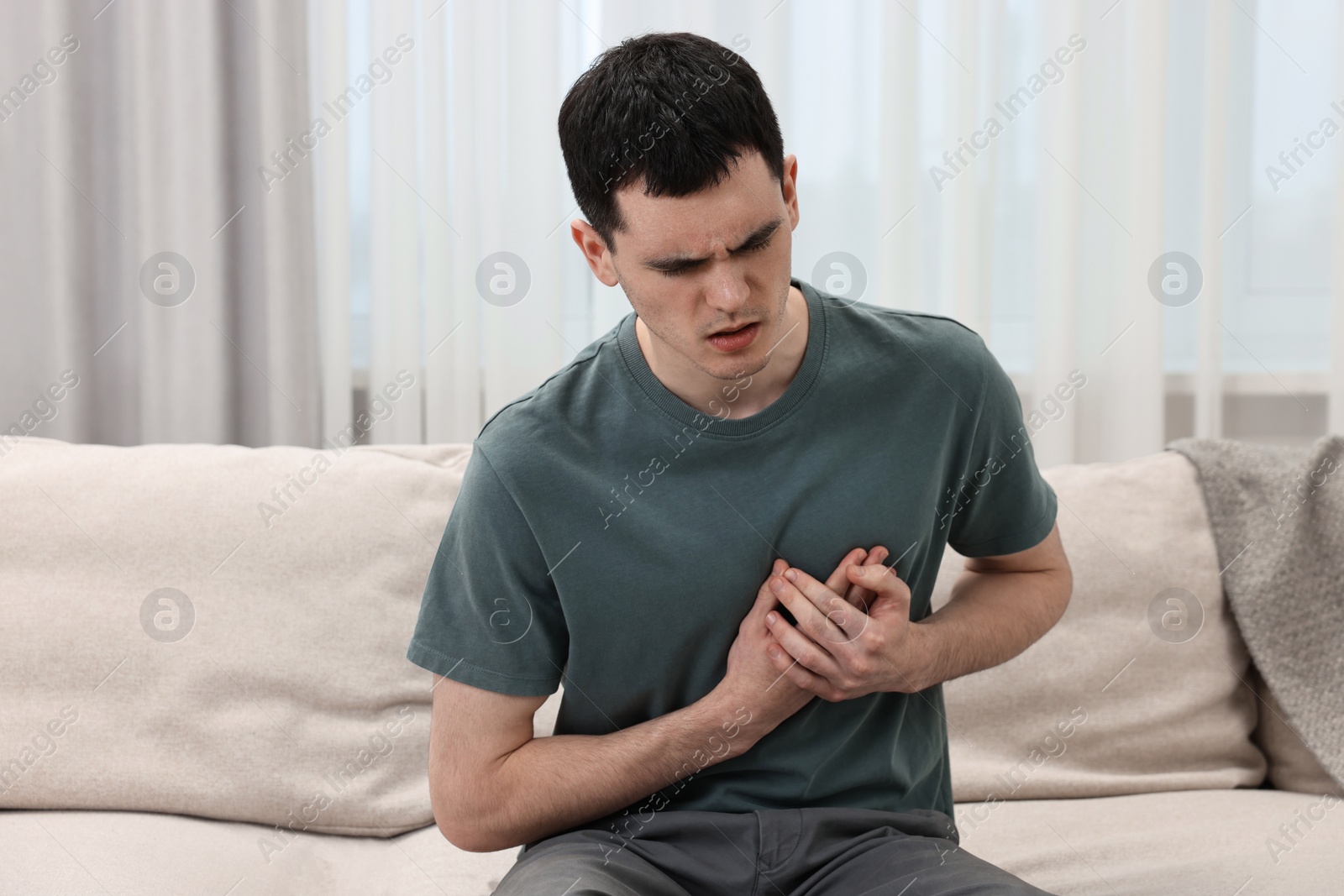 Photo of Young man suffering from heart hurt on sofa at home