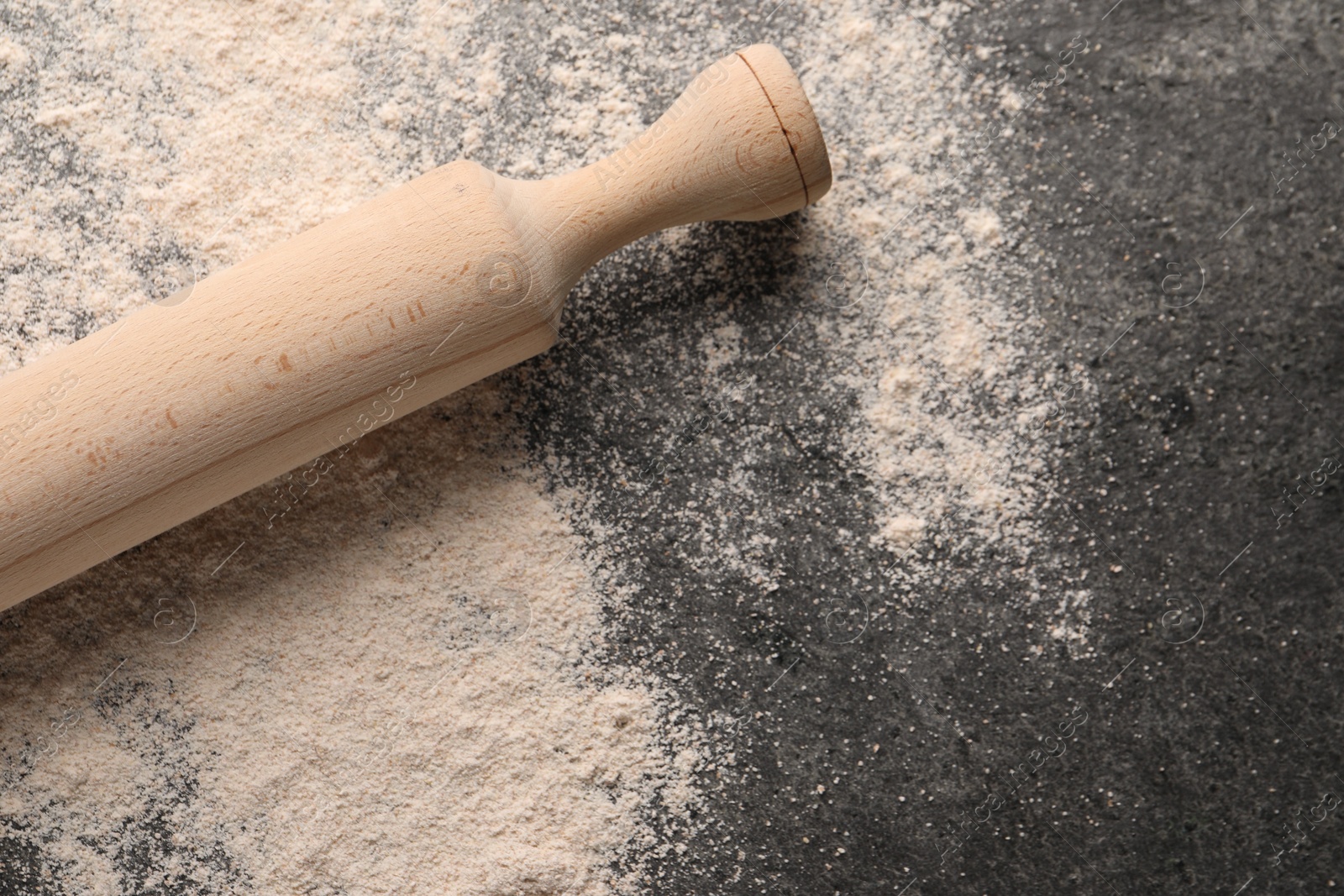 Photo of Scattered flour and rolling pin on grey textured table, top view