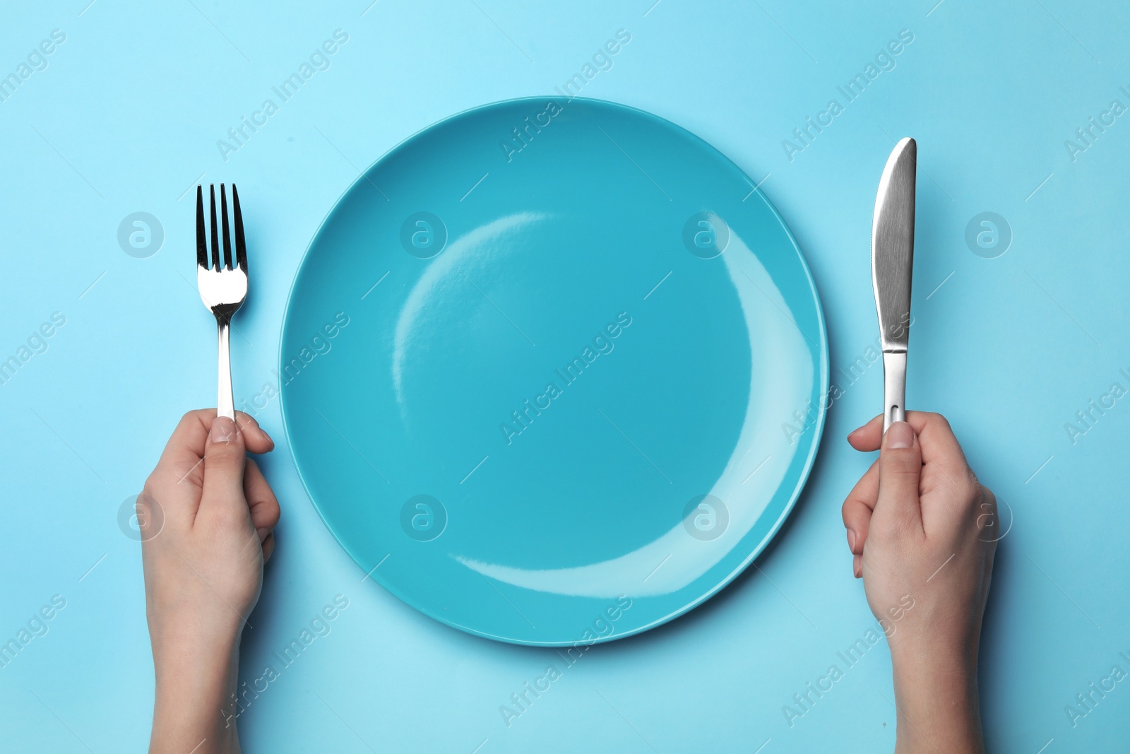 Photo of Woman with fork, knife and empty plate on color background, top view