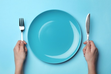 Woman with fork, knife and empty plate on color background, top view