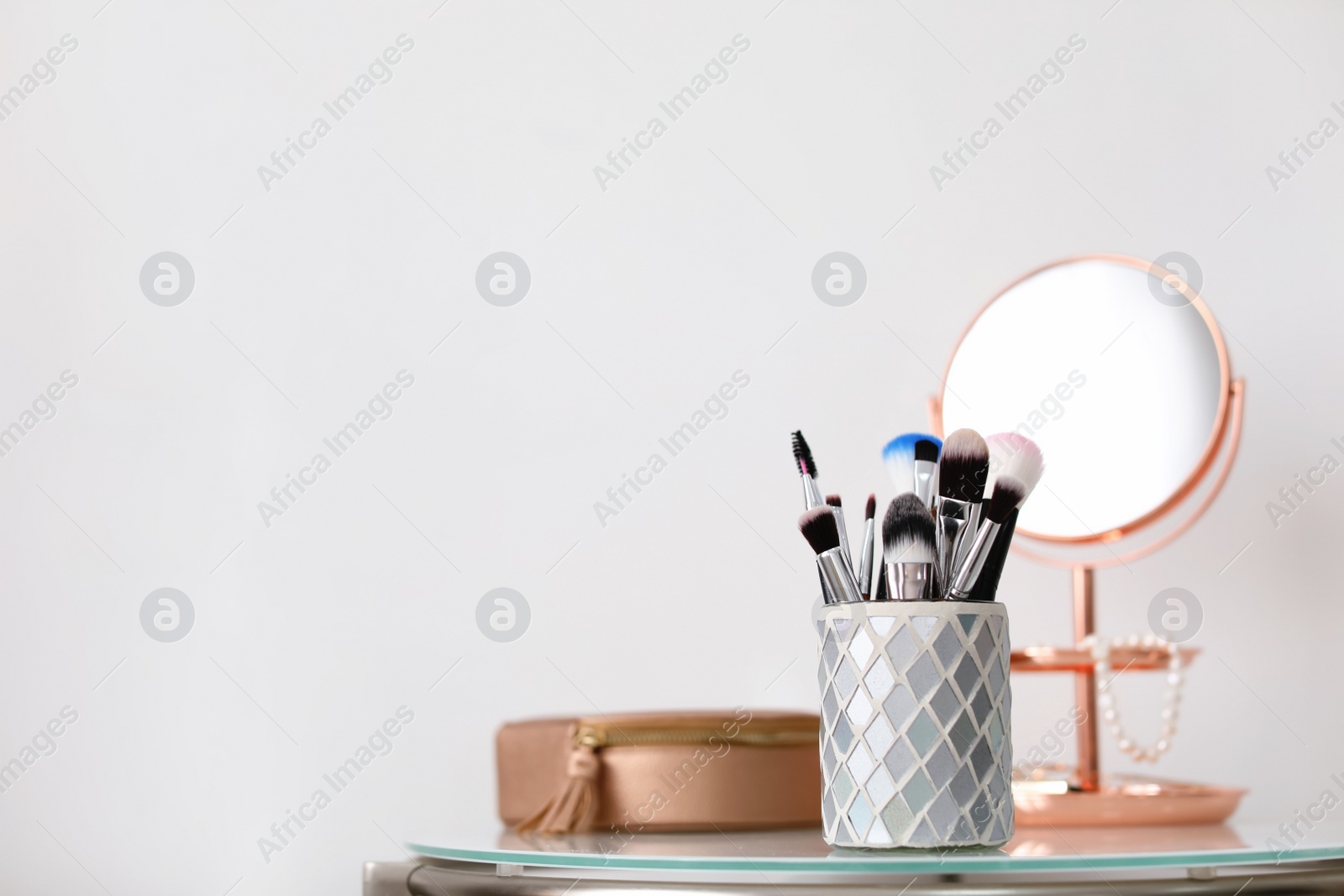 Photo of Makeup brushes in holder on table against light background