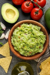 Delicious guacamole with nachos chips and ingredients on grey table, flat lay