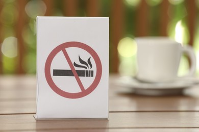 Photo of No Smoking sign and cup of drink on wooden table against blurred background, closeup