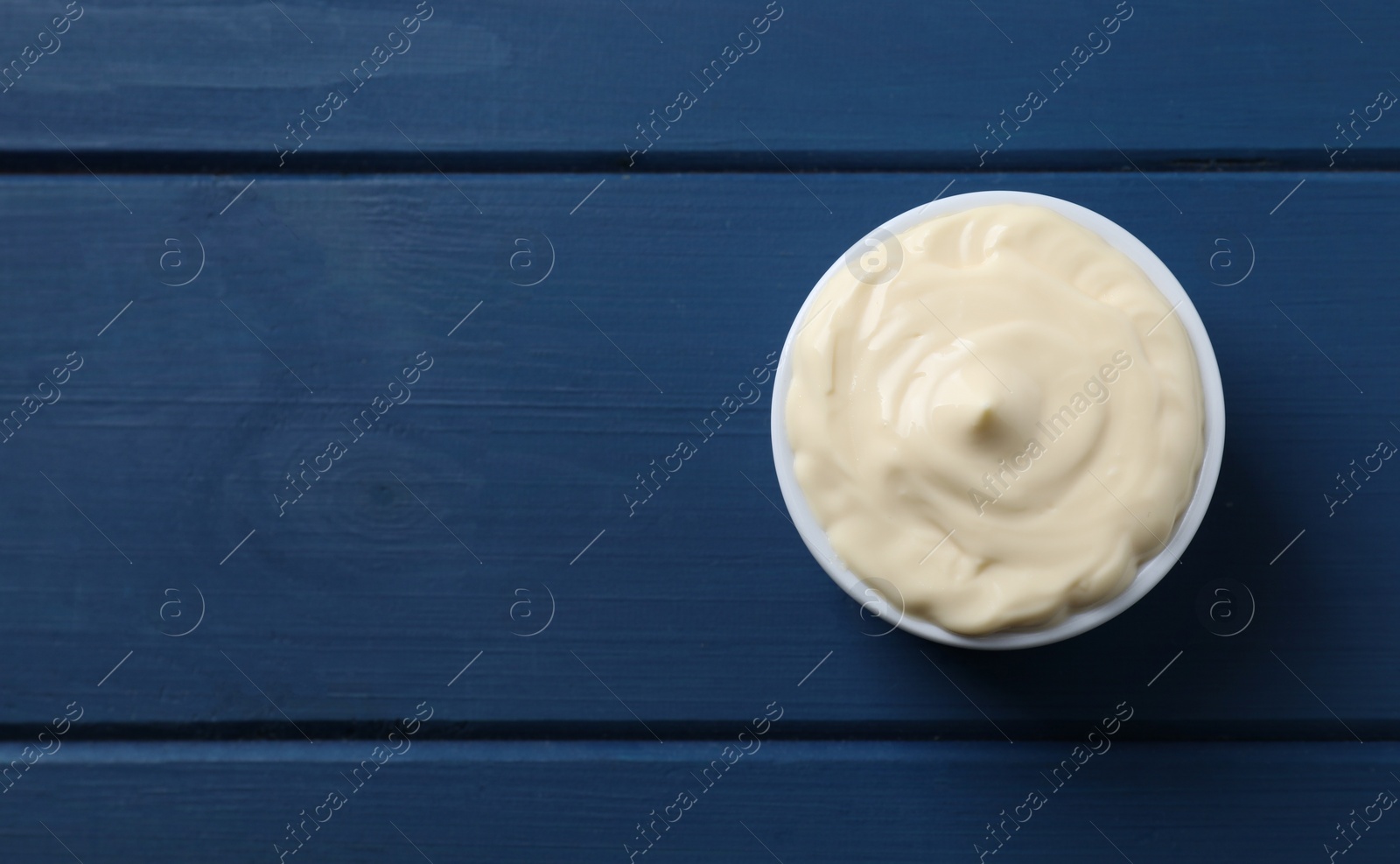 Photo of Tasty mayonnaise in bowl on blue wooden table, top view. Space for text