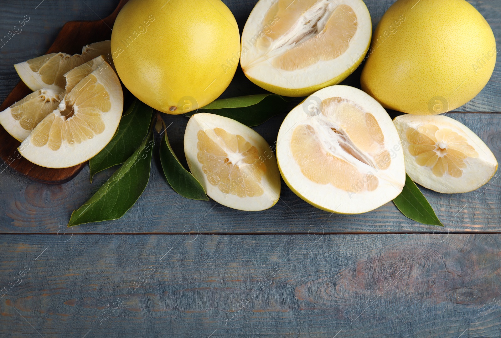 Photo of Fresh cut and whole pomelo fruits with leaves on blue wooden table, flat lay. Space for text