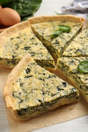 Cut delicious spinach pie on white wooden table, closeup