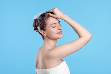 Happy young woman washing her hair with shampoo on light blue background