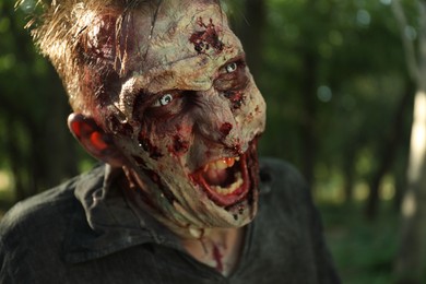 Photo of Scary zombie with bloody face outdoors, closeup. Halloween monster