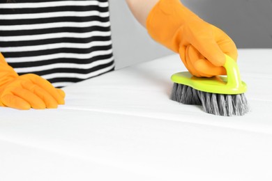 Woman in orange gloves cleaning white mattress with brush indoors, closeup