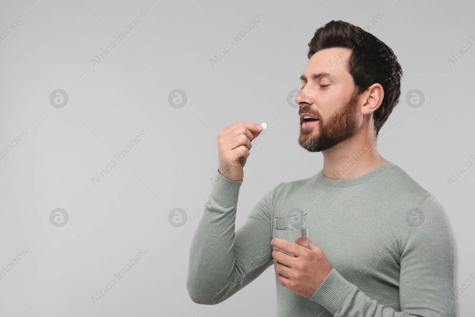 Photo of Handsome man with glass of water taking pill on light grey background, space for text