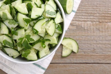 Delicious cucumber salad in bowl on wooden table, flat lay. Space for text