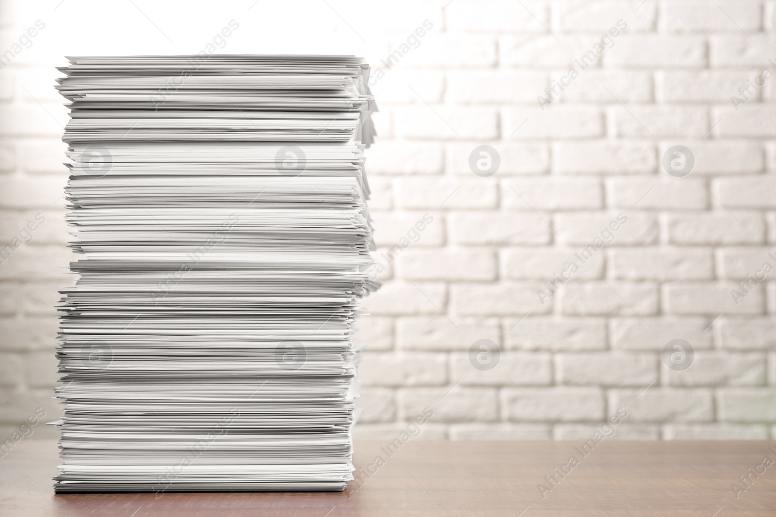 Photo of Stack of paper sheets on wooden table near white brick wall, space for text