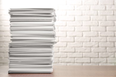 Photo of Stack of paper sheets on wooden table near white brick wall, space for text