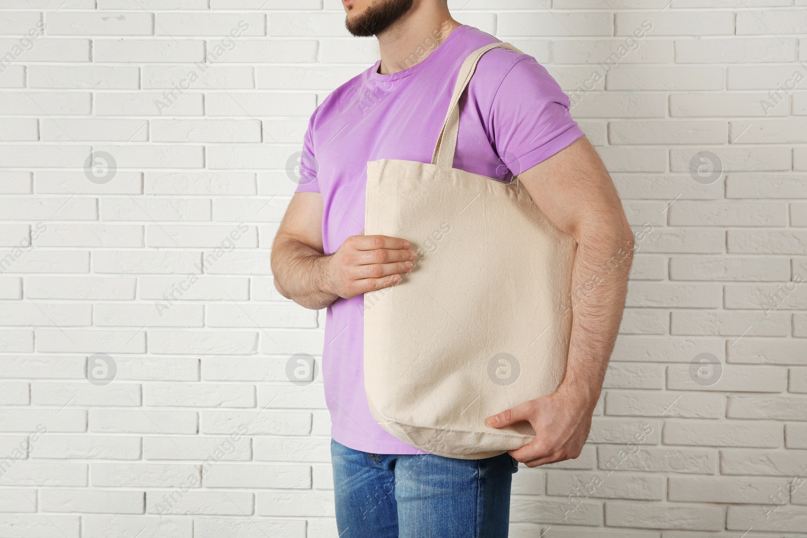 Photo of Man with cotton shopping eco bag against brick wall. Mockup for design