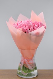 Bouquet of beautiful pink tulips in vase on wooden table against light grey background
