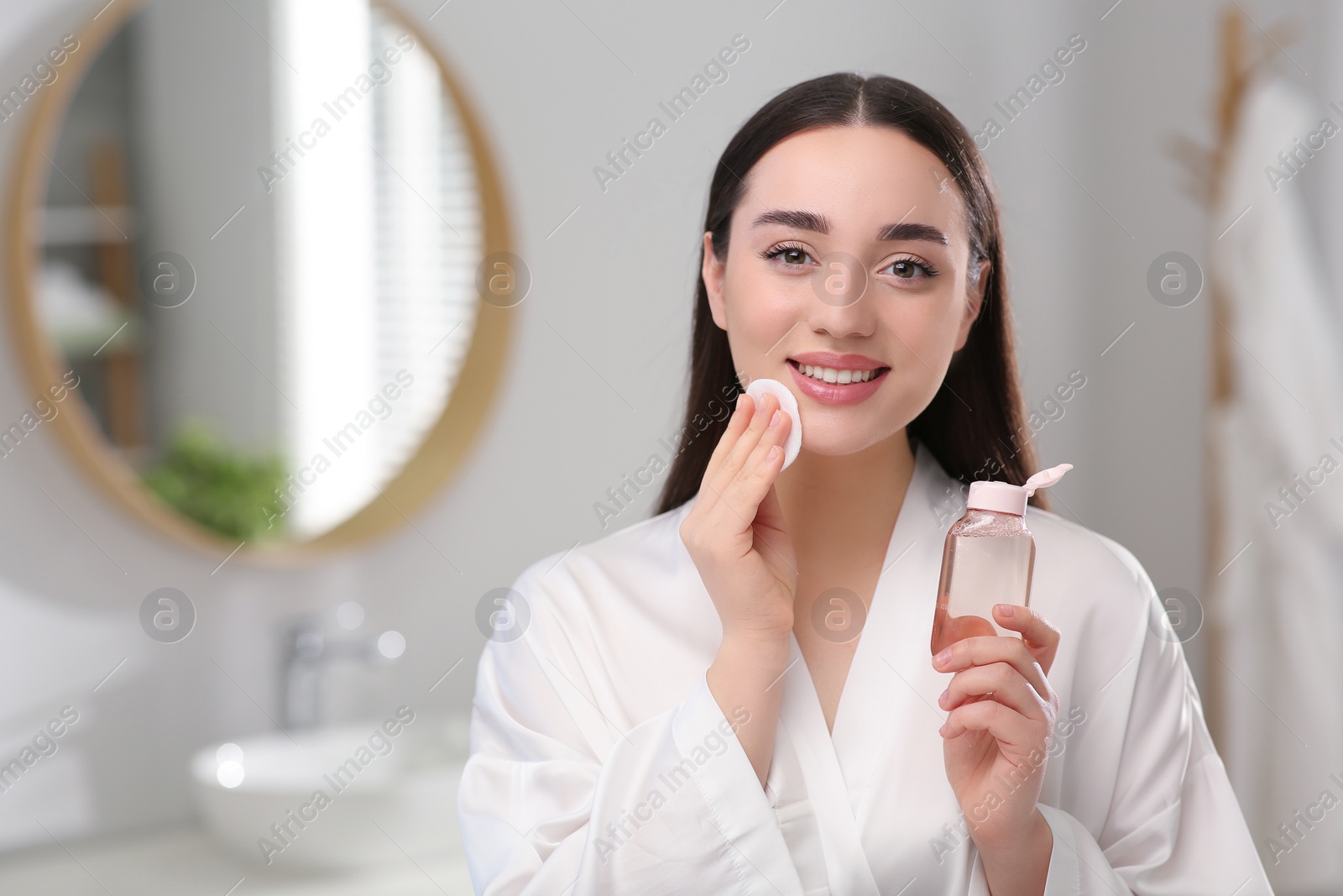 Photo of Beautiful woman removing makeup with cotton pad indoors