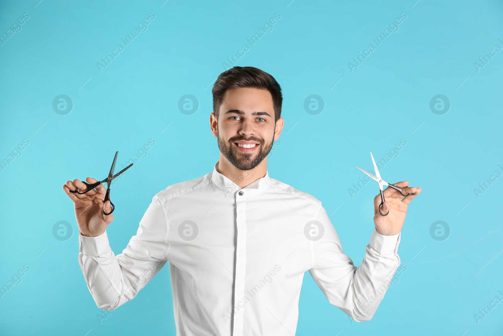 Photo of Young hairstylist holding professional scissors on color background