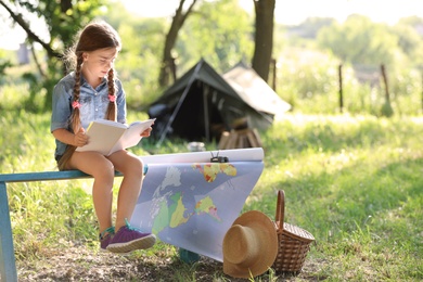 Photo of Little girl with map and book near tent outdoors. Summer camp