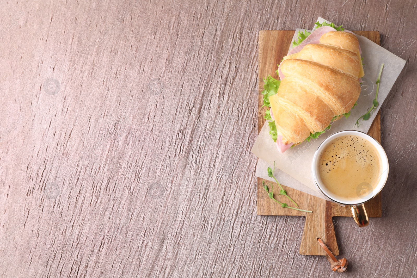 Photo of Tasty croissant sandwich with ham and cup of coffee on brown table, top view. Space for text