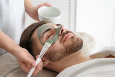 Photo of Cosmetologist applying mask on client's face in spa salon