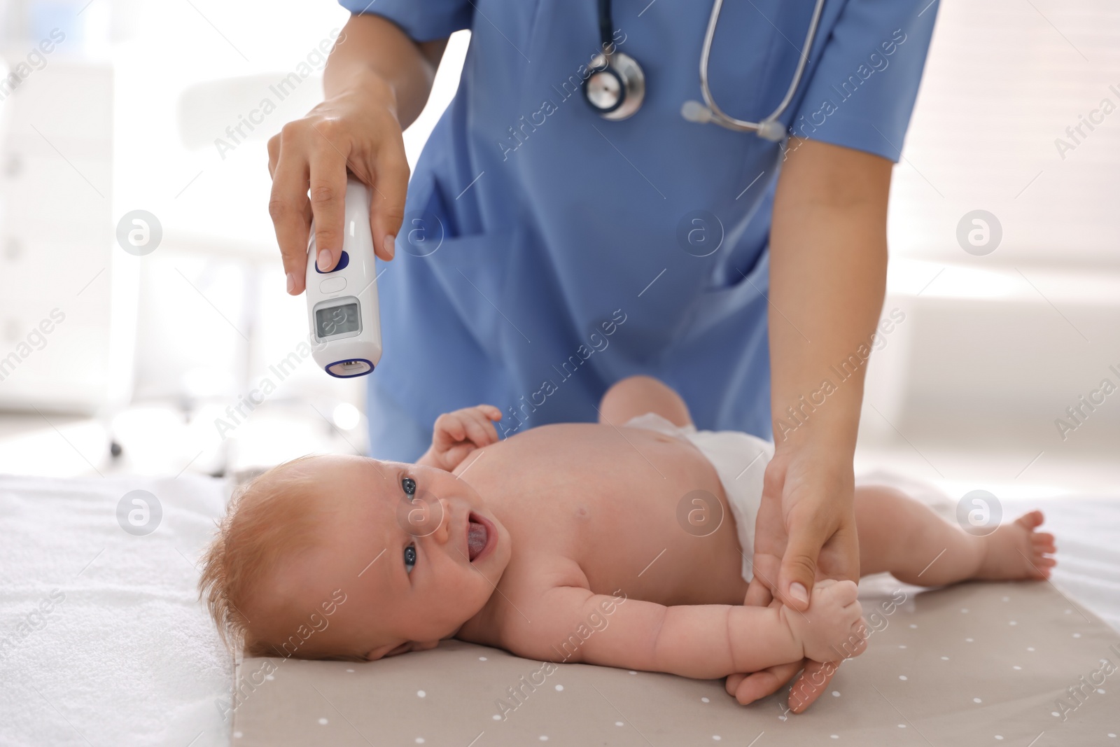 Photo of Doctor measuring temperature of little baby with non-contact thermometer in clinic, closeup. Health care