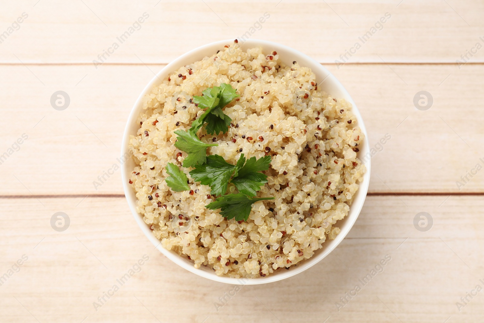 Photo of Tasty quinoa porridge with parsley in bowl on light wooden table, top view