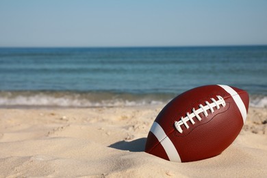 Photo of American football ball on beach. Space for text