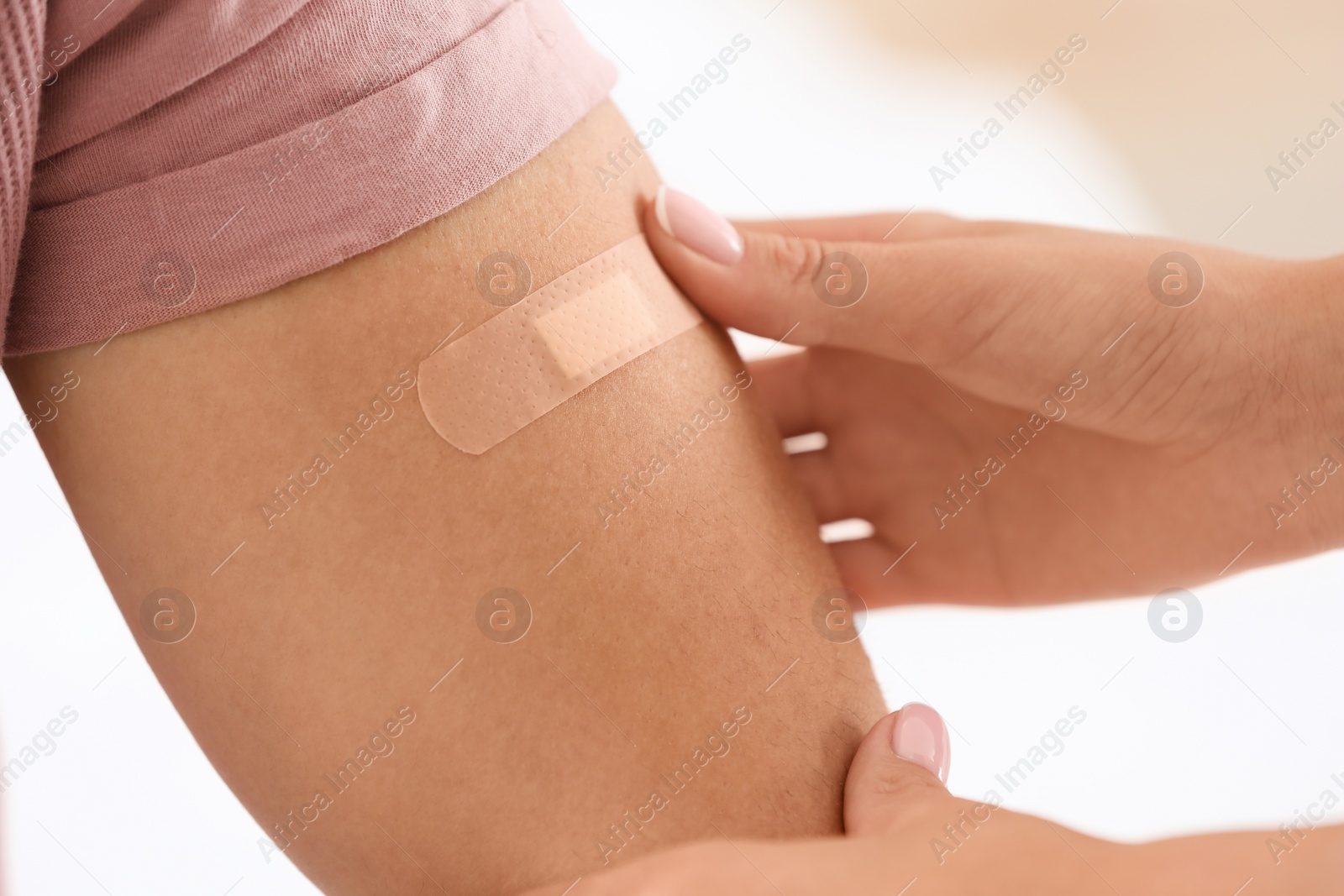 Photo of Woman applying adhesive bandage on man's arm against light background, closeup