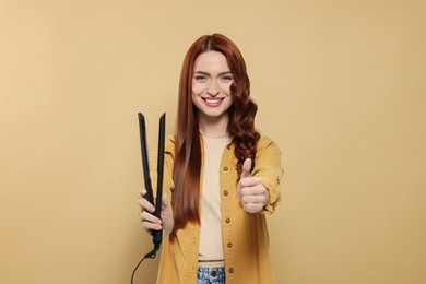Photo of Beautiful woman with hair iron showing thumbs up on beige background