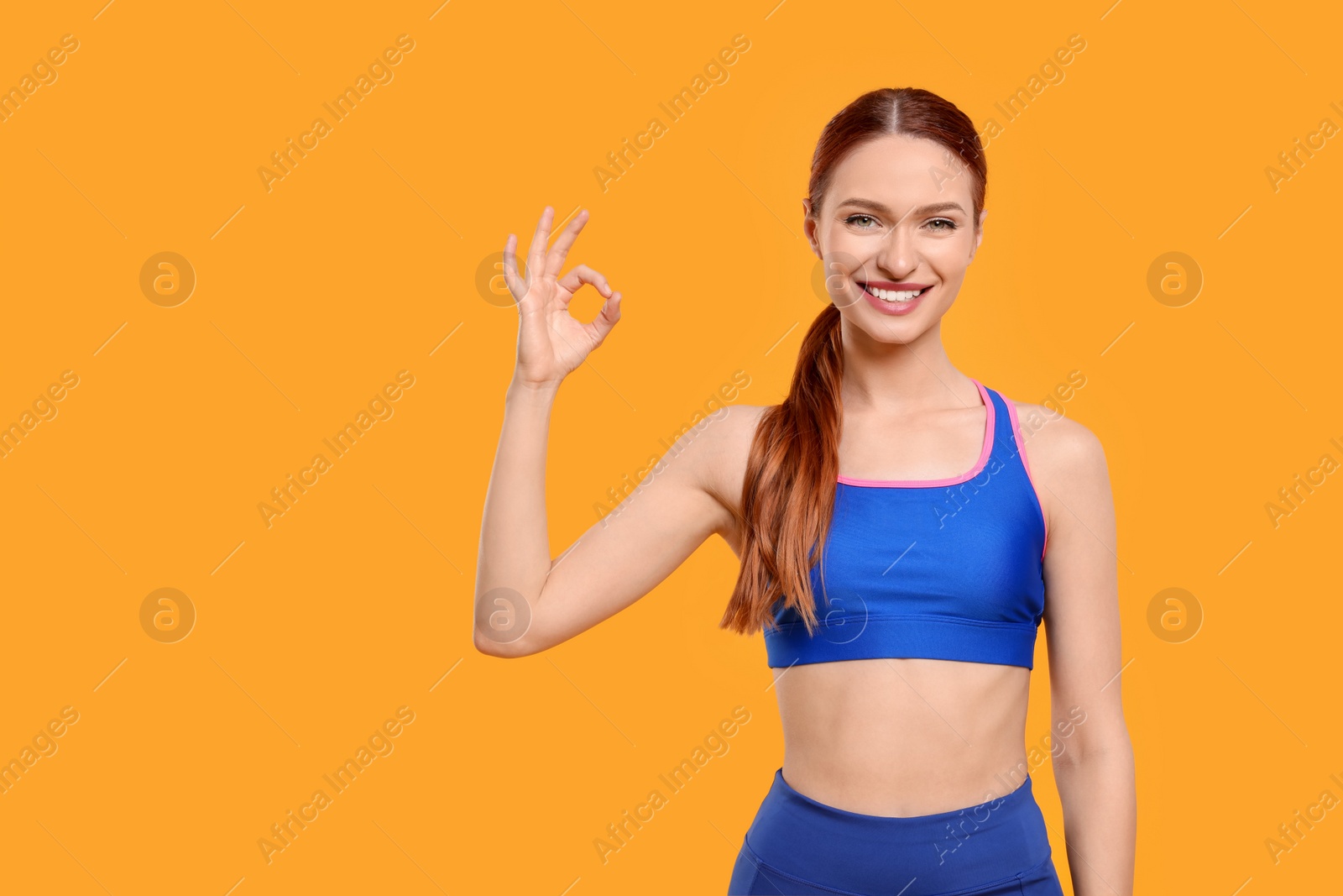 Photo of Young woman in sportswear showing OK gesture on yellow background, space for text