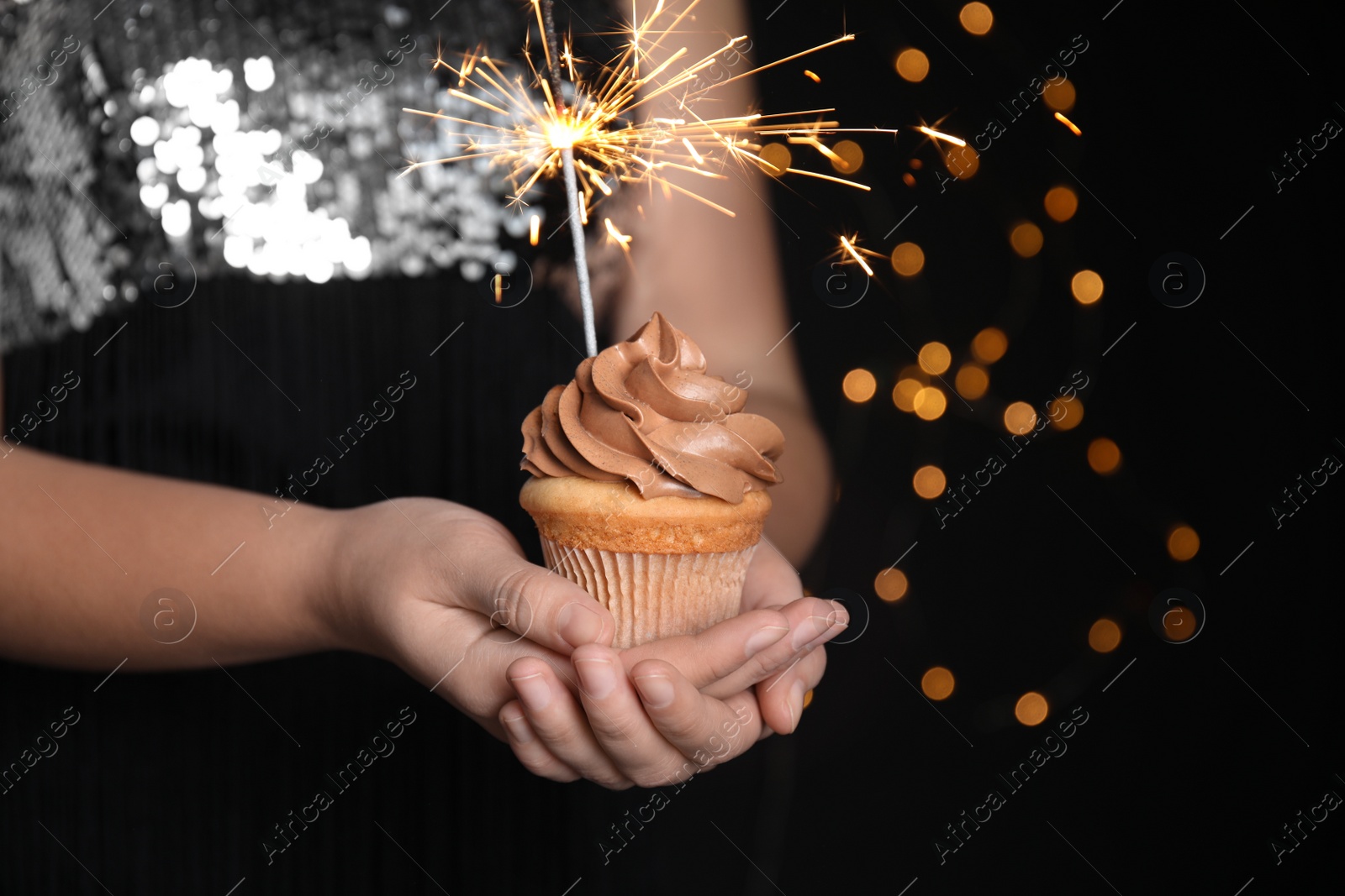 Photo of Woman holding birthday cupcake with sparkler on blurred background, closeup