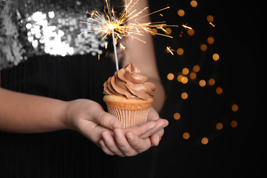 Woman holding birthday cupcake with sparkler on blurred background, closeup