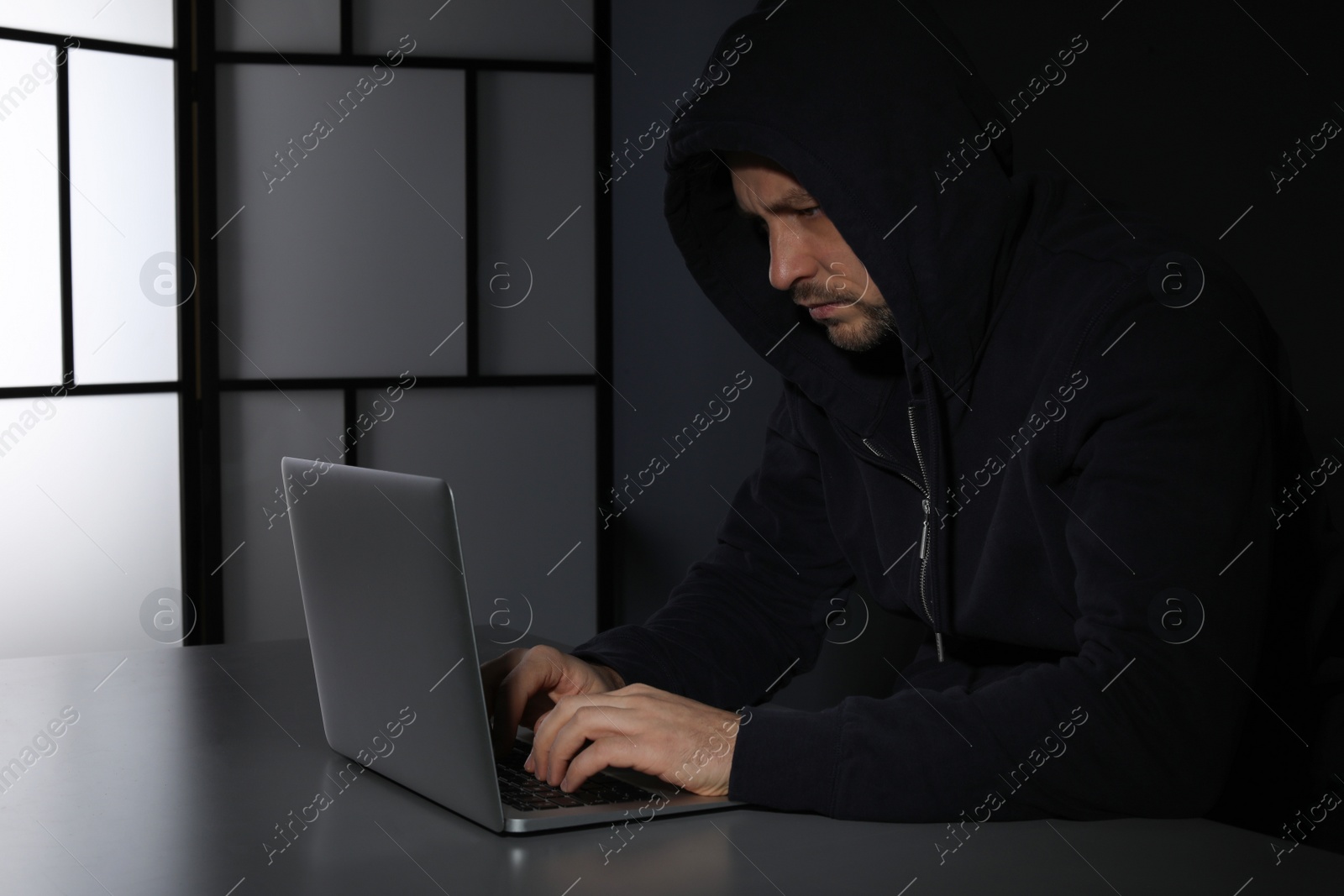 Photo of Man using laptop in dark room. Criminal offence