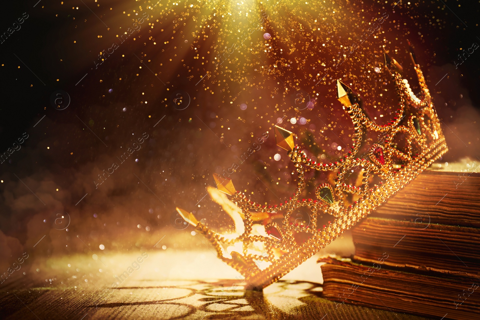 Image of Fantasy world. Beautiful golden crown and old books lit by magic light on table