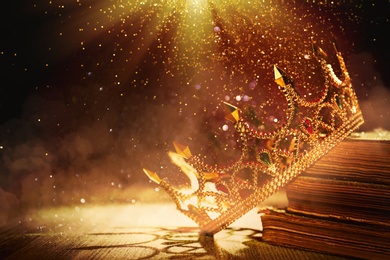 Image of Fantasy world. Beautiful golden crown and old books lit by magic light on table