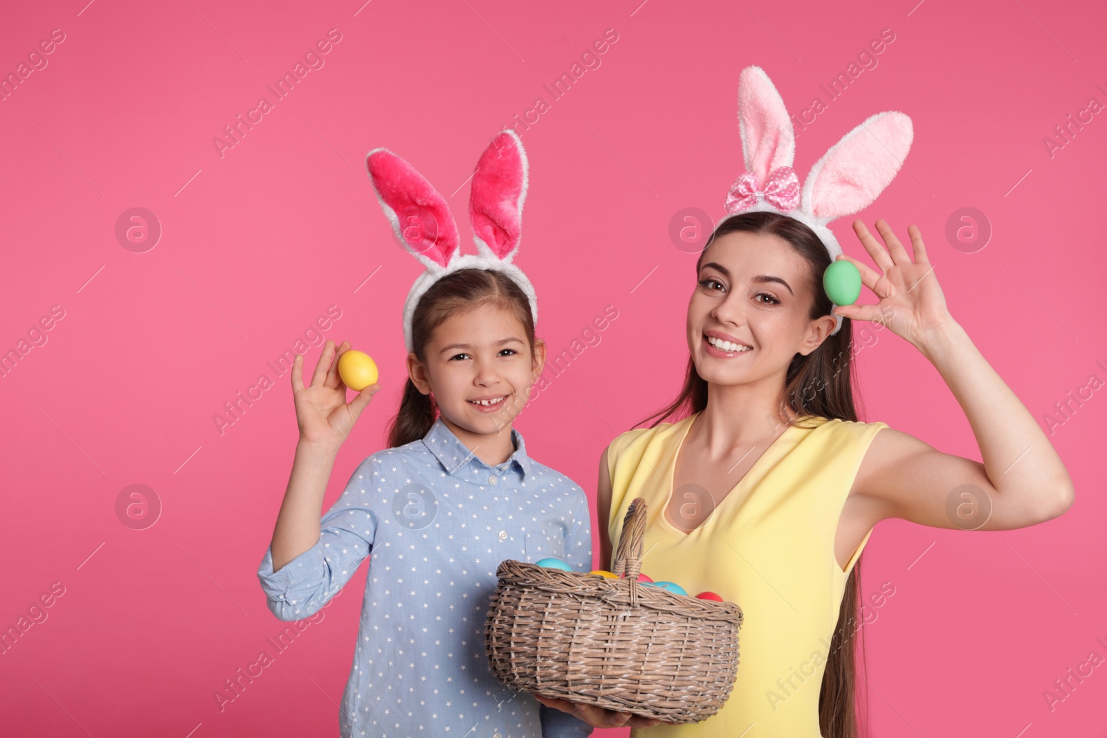 Photo of Mother and daughter in bunny ears headbands with Easter eggs on color background