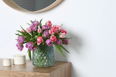 Beautiful bouquet of colorful tulip flowers on wooden chest of drawers near white wall. Space for text