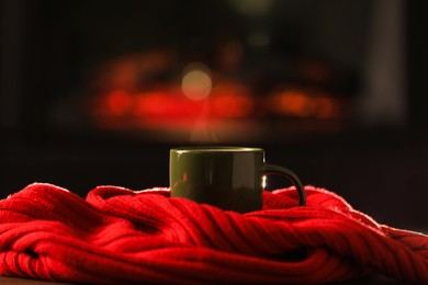Cup of hot drink and red knitted scarf on wooden table indoors. Cozy atmosphere