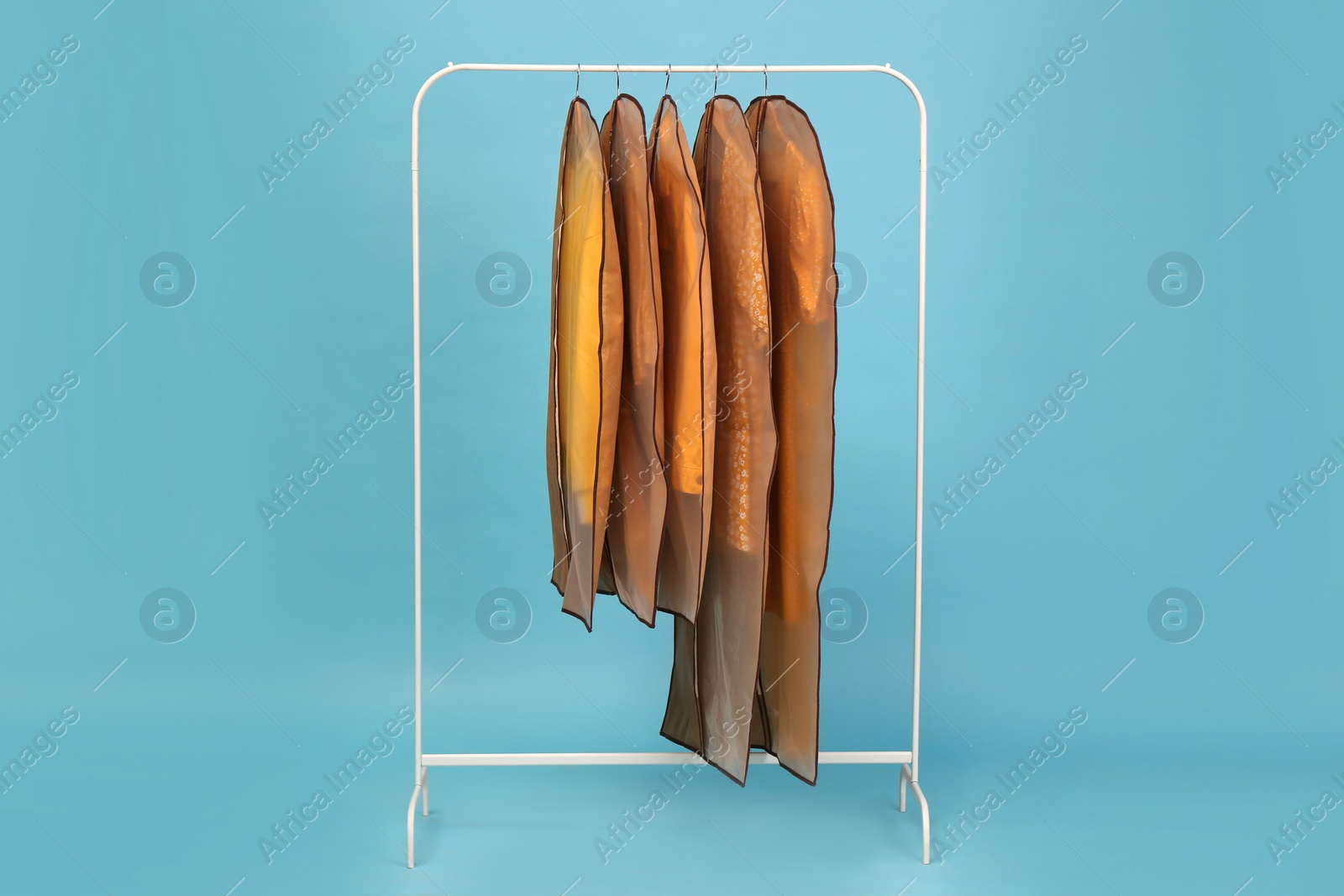 Photo of Garment bags with clothes on rack against light blue background