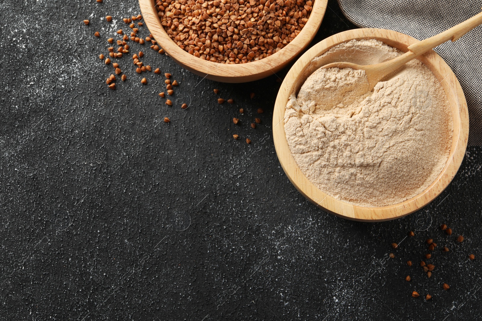 Photo of Buckwheat flour and grains in bowls on black table, flat lay. Space for text