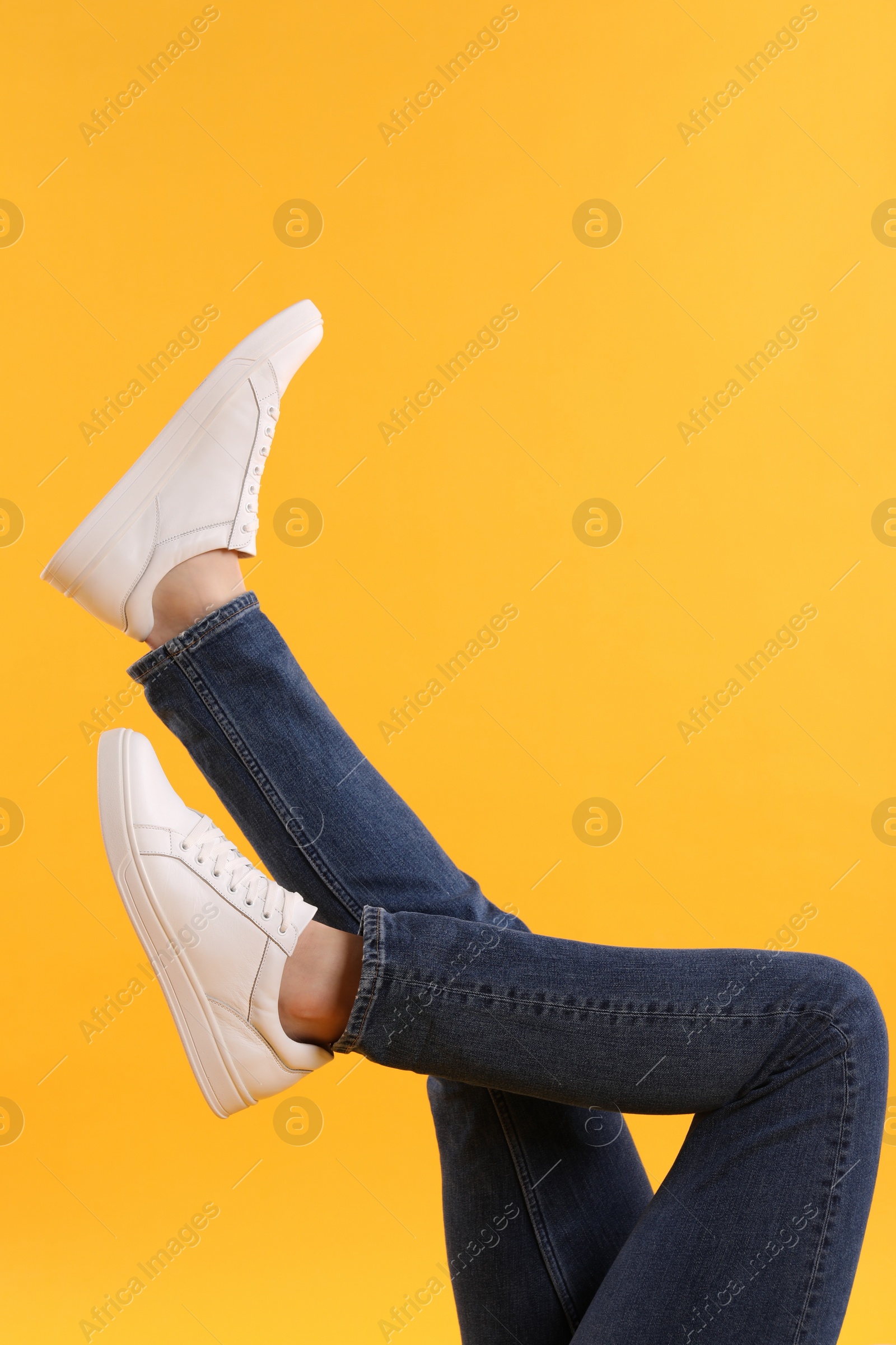 Photo of Man wearing stylish white sneakers on yellow background, closeup