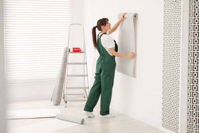 Woman hanging stylish gray wallpaper in room