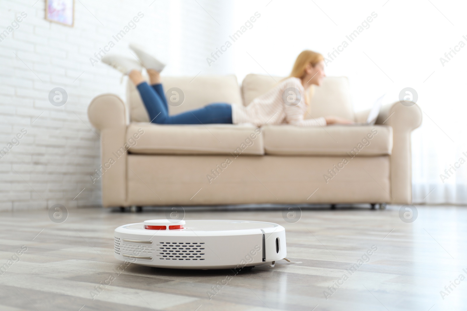 Photo of Woman resting while robotic vacuum cleaner doing her work at home