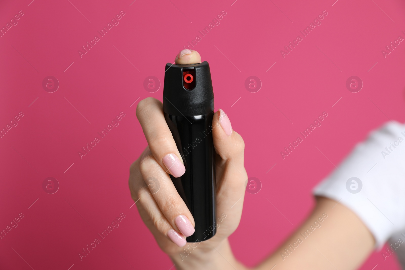 Photo of Young woman using pepper spray on pink background, closeup