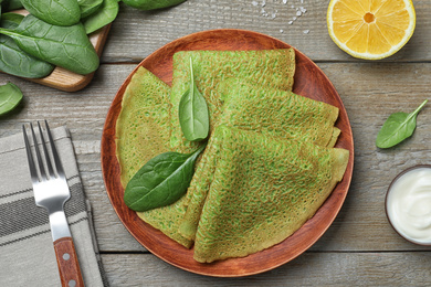 Delicious spinach crepes served on wooden table, flat lay