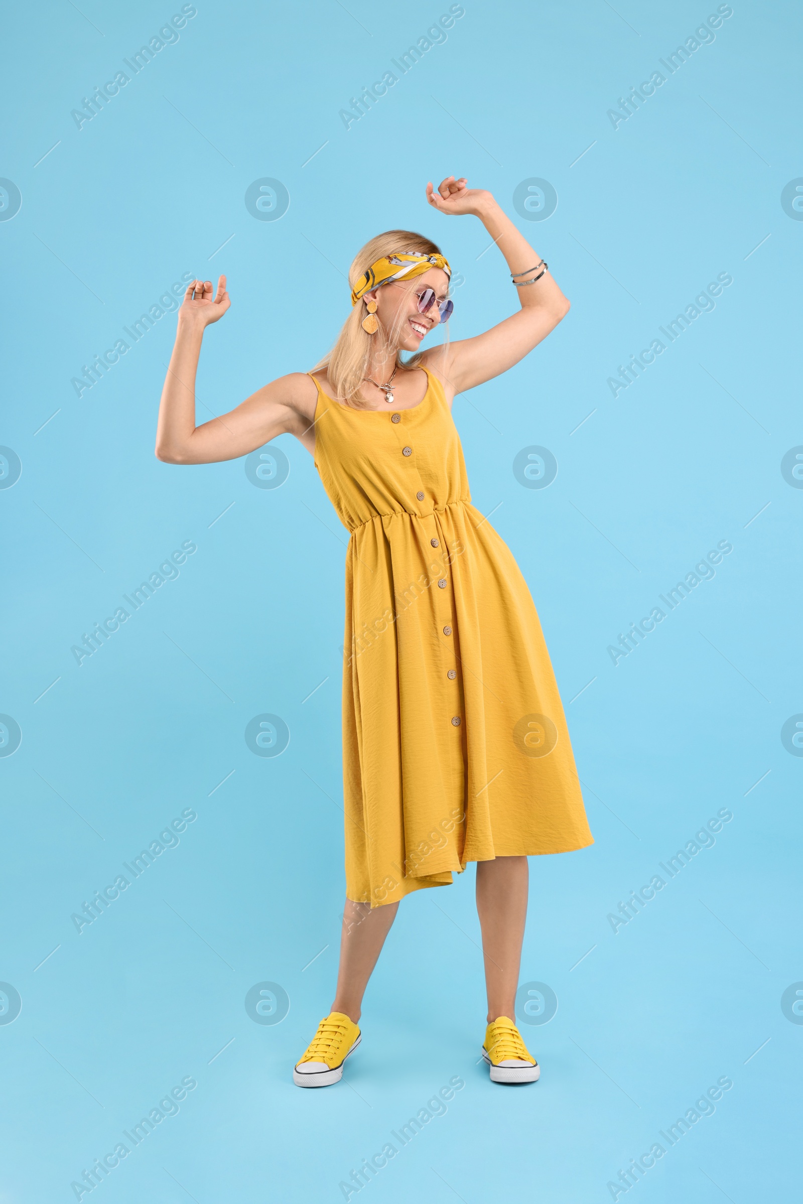 Photo of Portrait of smiling hippie woman dancing on light blue background