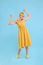 Portrait of smiling hippie woman dancing on light blue background